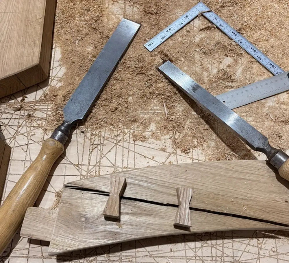 Chisels, a steel square and a shaped oak rail laid out on a plywood scribing floor covered in layout lines.