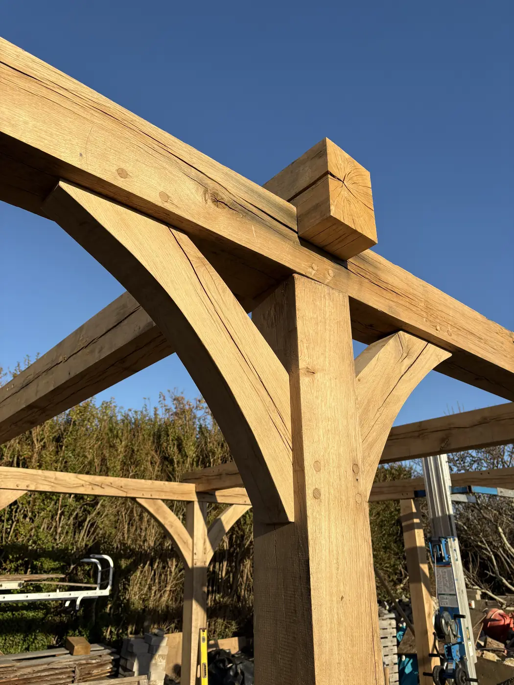 Curved oak braces meeting a post head and tie beam against blue sky.