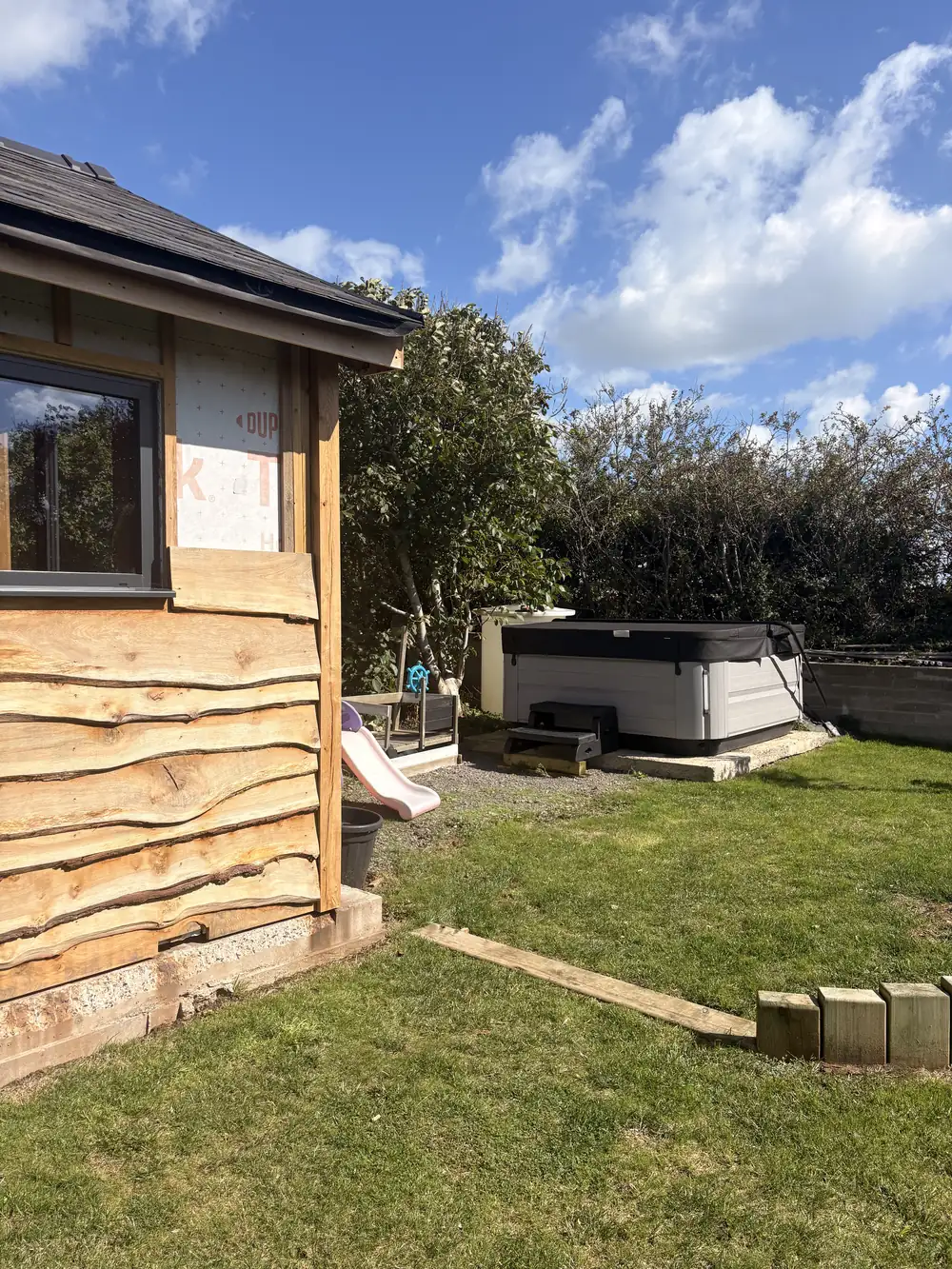 An oak framed building clad in waney-edge oak boards, seen from the garden.