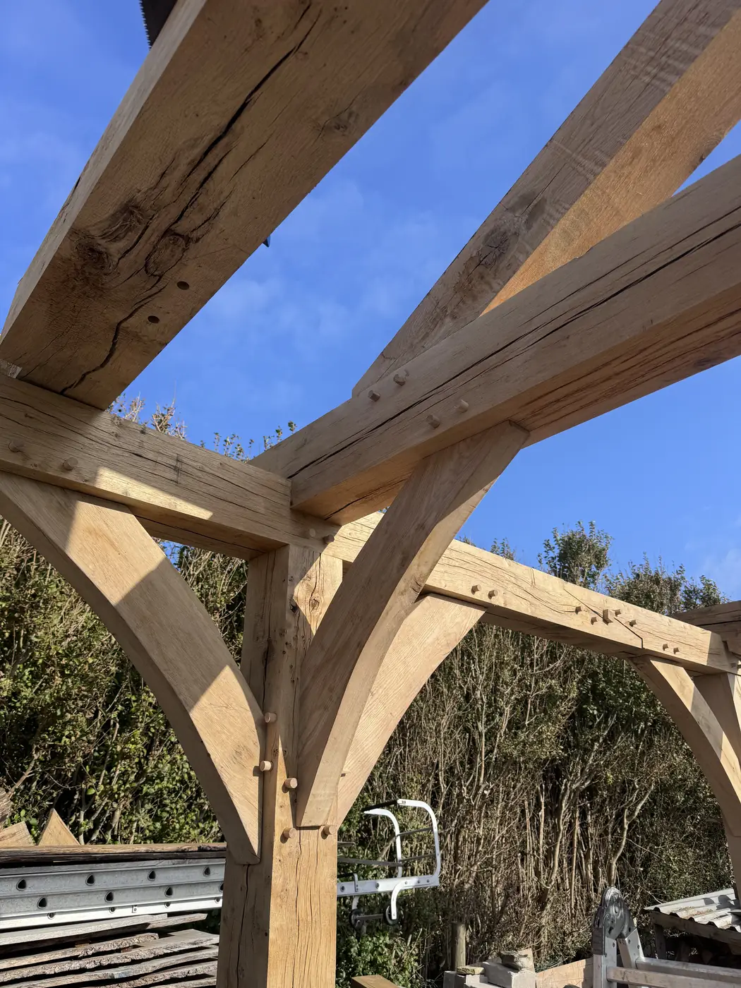 Looking up at a green oak frame from beneath, braces and beams crossing against blue sky.