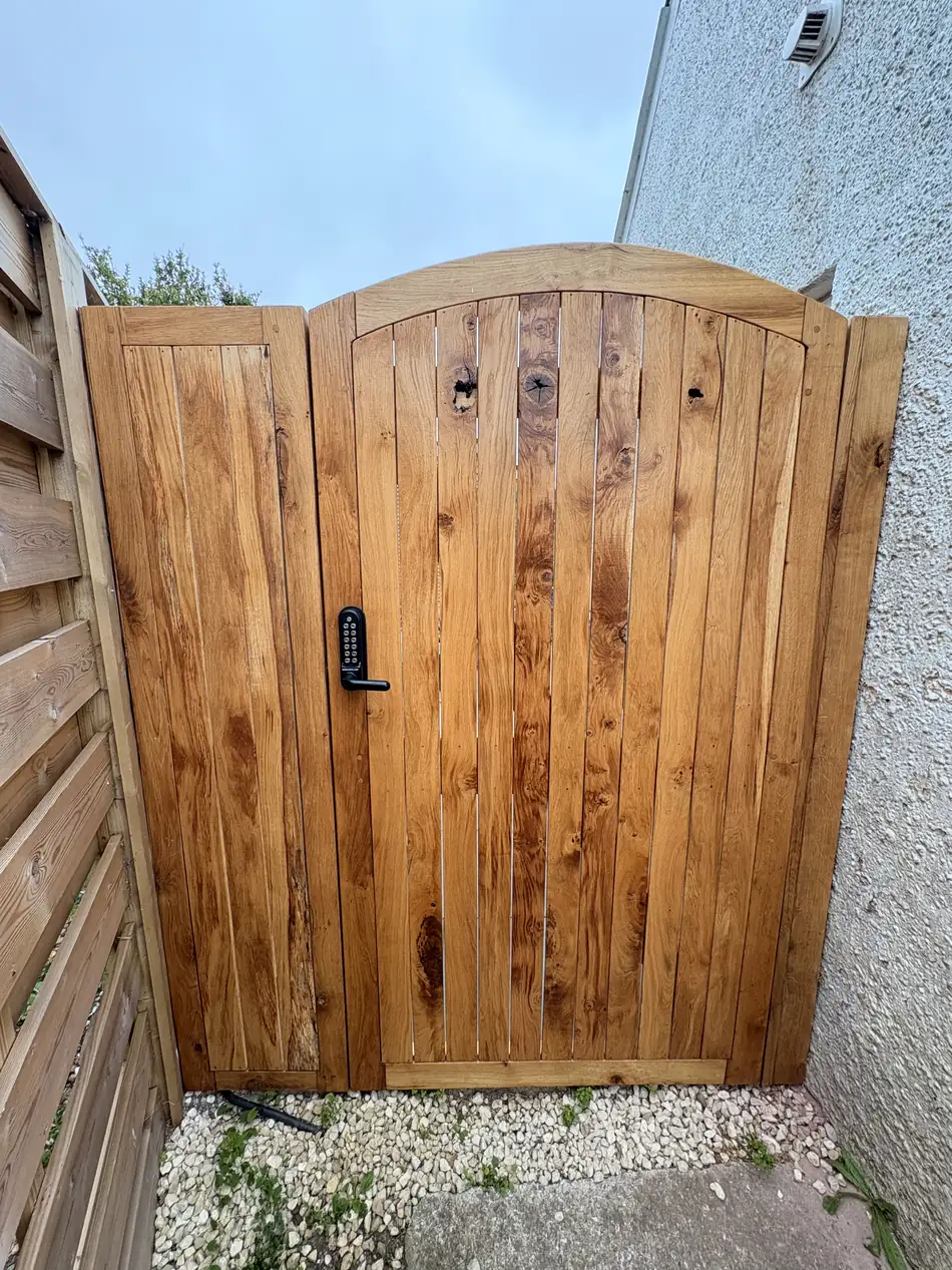 An arched braced oak gate hung in a stone opening, seen straight on.