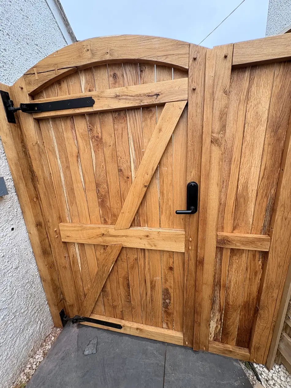 An arched oak gate at an angle showing the strap hinge and diagonal brace.