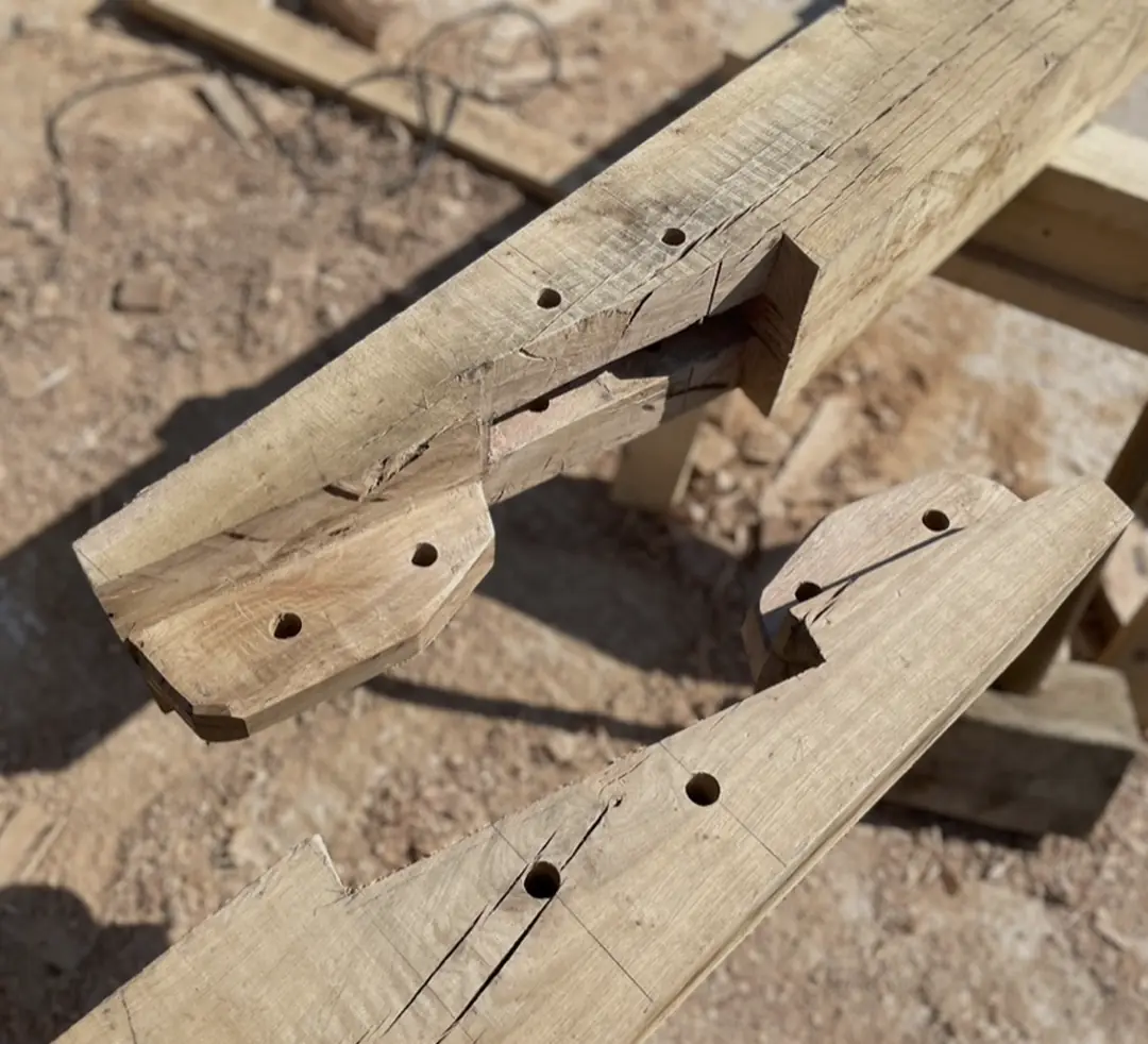 Two oak tenons cut on the ends of beams, laid on trestles, each drilled with draw-bore peg holes.