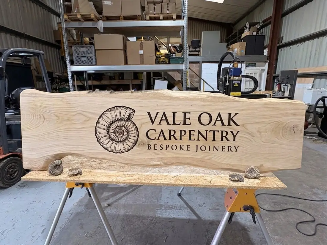 A live-edge oak sign engraved with lettering and an ammonite motif.